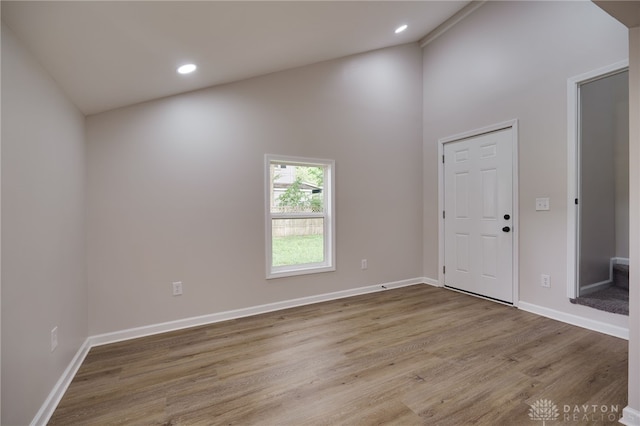 empty room with recessed lighting, wood finished floors, baseboards, and high vaulted ceiling