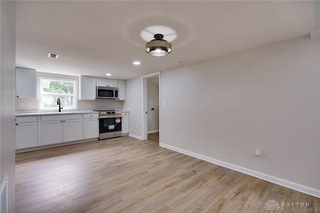 kitchen with baseboards, visible vents, light wood finished floors, a sink, and stainless steel appliances