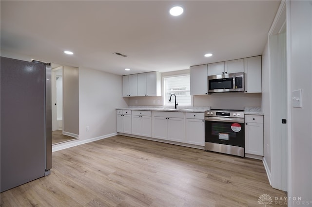 kitchen featuring light wood-type flooring, a sink, recessed lighting, appliances with stainless steel finishes, and light countertops