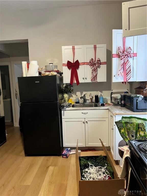 kitchen featuring white cabinets, sink, light hardwood / wood-style floors, and black appliances