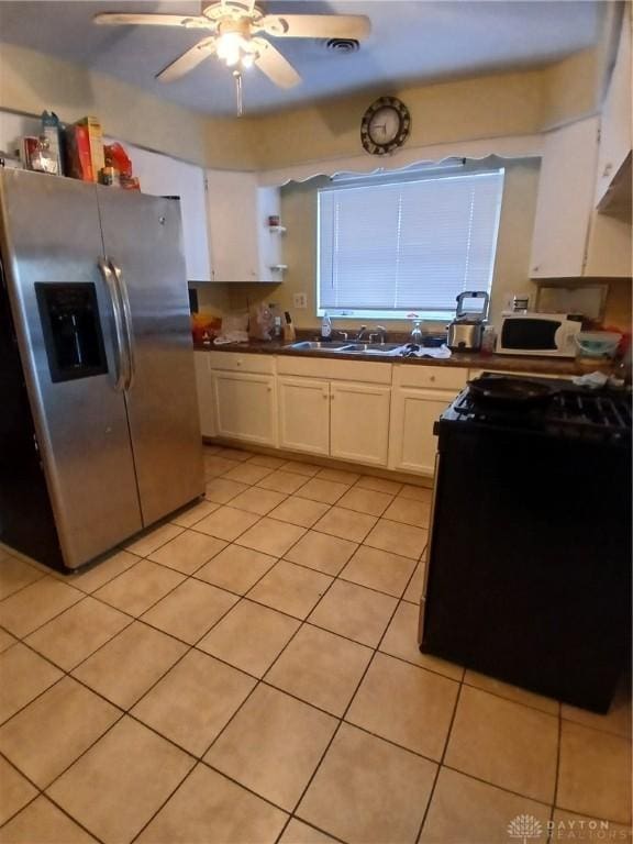 kitchen with light tile patterned flooring, sink, white cabinets, stainless steel fridge, and black range