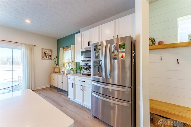 kitchen featuring appliances with stainless steel finishes, white cabinets, a textured ceiling, and light hardwood / wood-style floors