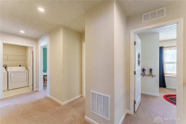 corridor featuring separate washer and dryer, light carpet, and a textured ceiling