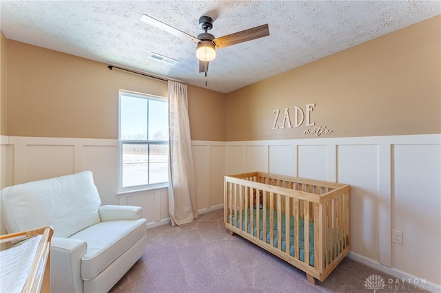 bedroom with ceiling fan, a textured ceiling, carpet, and a crib