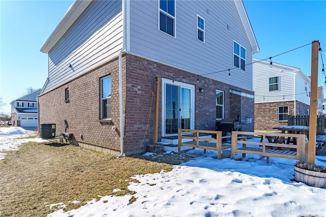 snow covered rear of property featuring central AC unit