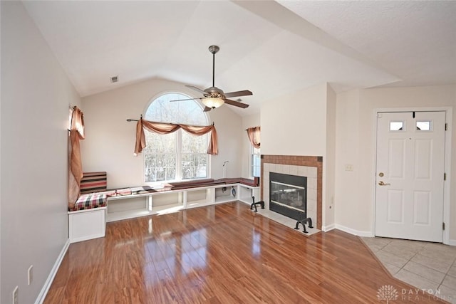 unfurnished living room featuring a tiled fireplace, ceiling fan, lofted ceiling, and light hardwood / wood-style floors