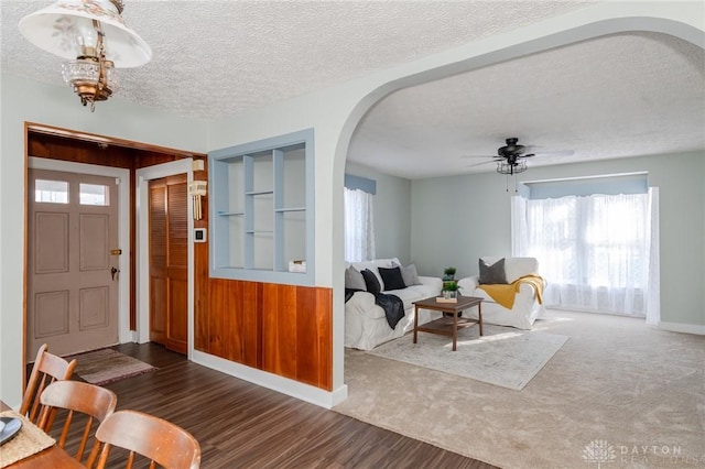 foyer entrance with a healthy amount of sunlight, ceiling fan with notable chandelier, dark wood-type flooring, and a textured ceiling