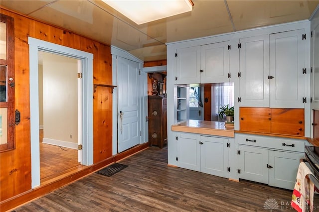 kitchen with dark wood-type flooring, wooden walls, electric range oven, and white cabinets