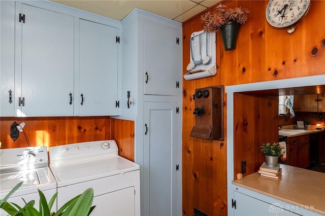 laundry area with cabinets, wooden walls, separate washer and dryer, and sink