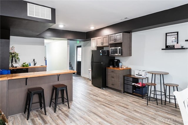 kitchen with wood counters, a breakfast bar, light hardwood / wood-style flooring, black refrigerator, and kitchen peninsula