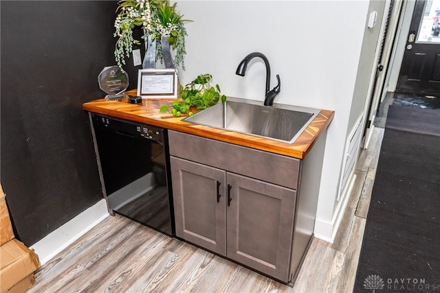 kitchen featuring butcher block countertops, sink, light hardwood / wood-style floors, and black dishwasher