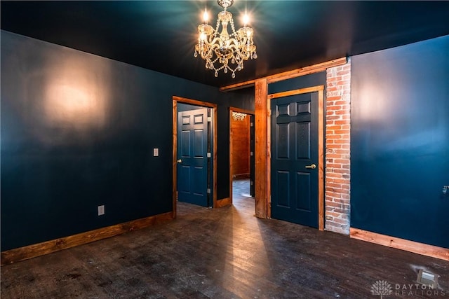 unfurnished room featuring an inviting chandelier, wood finished floors, and baseboards