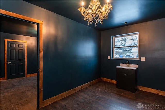 empty room with dark wood finished floors, a notable chandelier, baseboards, and a sink