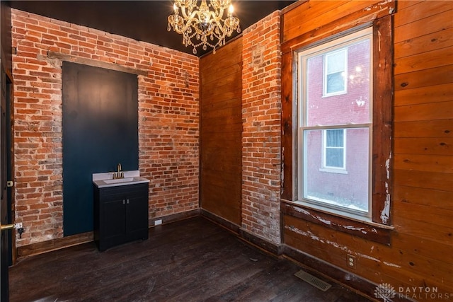 unfurnished room with brick wall, wooden walls, sink, a chandelier, and dark wood-type flooring