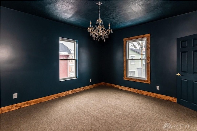 empty room with an inviting chandelier, baseboards, carpet floors, and a textured ceiling