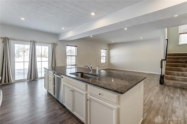 kitchen with sink, dishwasher, a kitchen island with sink, white cabinetry, and dark stone counters