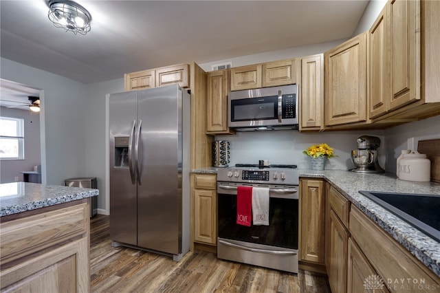 kitchen with dark wood-type flooring, ceiling fan, appliances with stainless steel finishes, light stone countertops, and light brown cabinetry