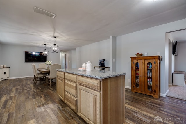 kitchen with dark hardwood / wood-style floors, decorative light fixtures, a center island, a notable chandelier, and light stone countertops