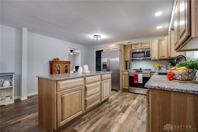 kitchen featuring sink, dark wood-type flooring, appliances with stainless steel finishes, a center island, and light stone counters