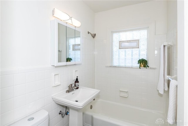 full bathroom featuring tiled shower / bath, toilet, sink, and tile walls