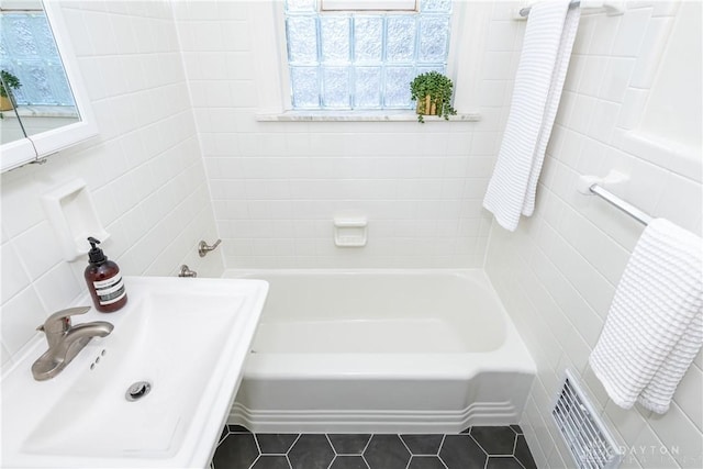 bathroom with tile patterned flooring, sink, a bath, and tile walls