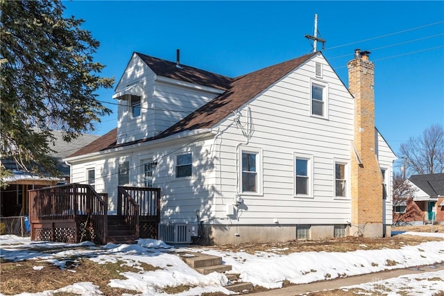 snow covered back of property with cooling unit and a wooden deck