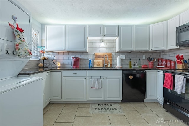 kitchen featuring sink, light tile patterned floors, stacked washing maching and dryer, white cabinetry, and black appliances