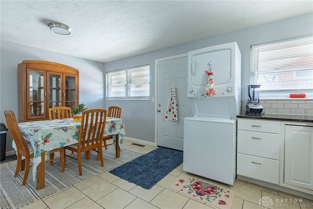 kitchen featuring light tile patterned floors, white cabinetry, stacked washer and clothes dryer, a textured ceiling, and decorative backsplash