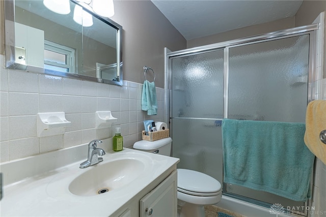 bathroom with a shower with door, tile walls, tasteful backsplash, vanity, and toilet