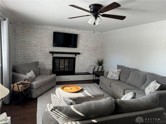 living room featuring dark wood-type flooring, ceiling fan, a fireplace, ornamental molding, and brick wall