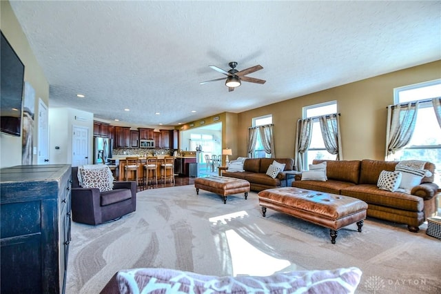 living room with ceiling fan, light colored carpet, and a textured ceiling