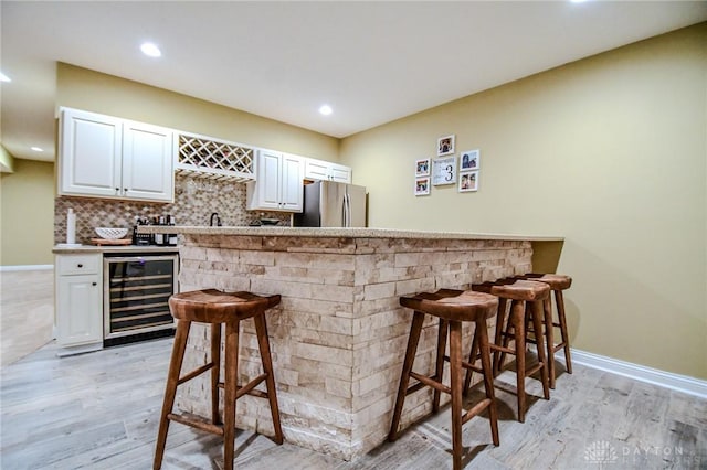 bar with tasteful backsplash, stainless steel fridge, white cabinets, beverage cooler, and light hardwood / wood-style floors