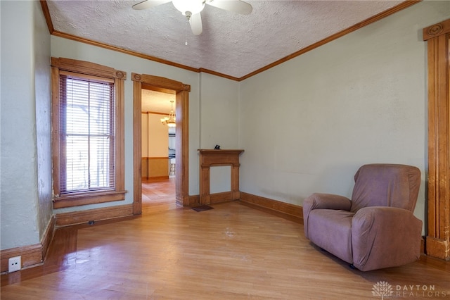 living area featuring ceiling fan, ornamental molding, light hardwood / wood-style floors, and a textured ceiling