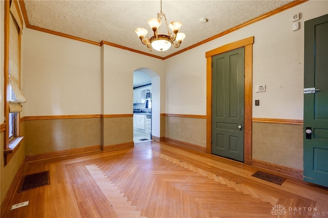 empty room with crown molding, an inviting chandelier, a textured ceiling, and light parquet floors