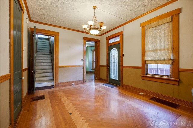 foyer entrance with light parquet floors, ornamental molding, a chandelier, and a textured ceiling