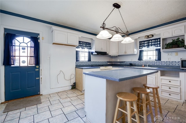 kitchen featuring pendant lighting, white cabinetry, ornamental molding, a textured ceiling, and a kitchen island