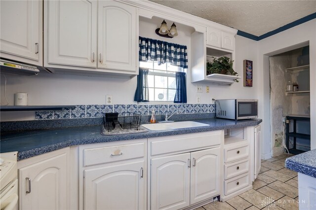 kitchen with sink, crown molding, a textured ceiling, white cabinets, and stove