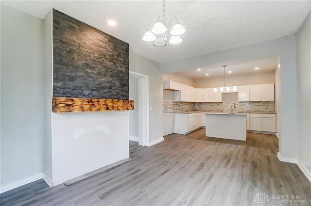 kitchen with decorative backsplash, a kitchen island with sink, white cabinets, and decorative light fixtures