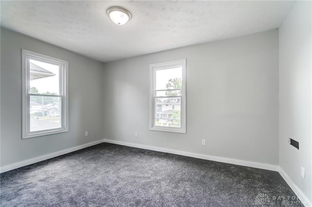 spare room featuring a wealth of natural light and dark carpet