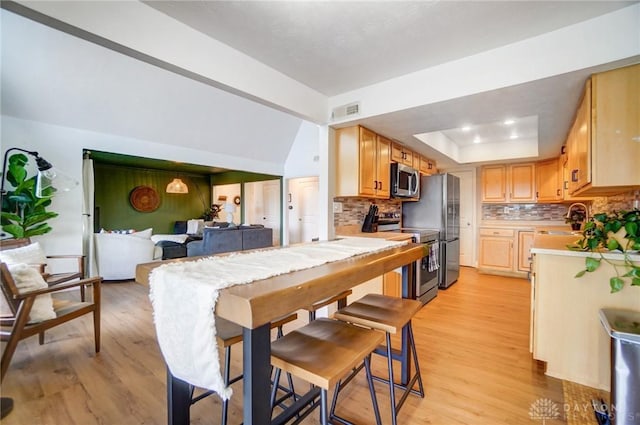 kitchen featuring tasteful backsplash, a tray ceiling, light hardwood / wood-style flooring, and appliances with stainless steel finishes