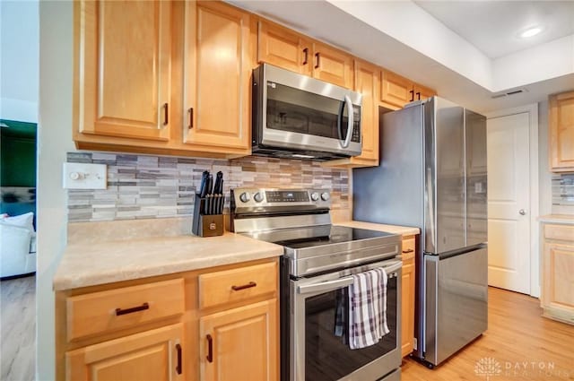 kitchen featuring tasteful backsplash, appliances with stainless steel finishes, light brown cabinetry, and light hardwood / wood-style floors