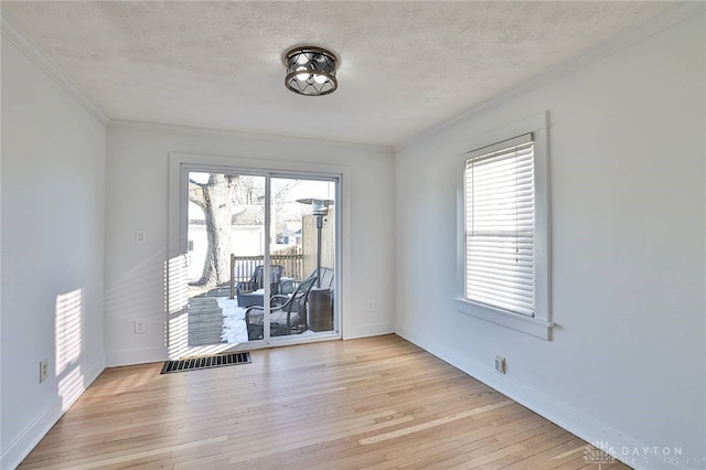 empty room with a wealth of natural light, ornamental molding, a textured ceiling, and light wood-type flooring