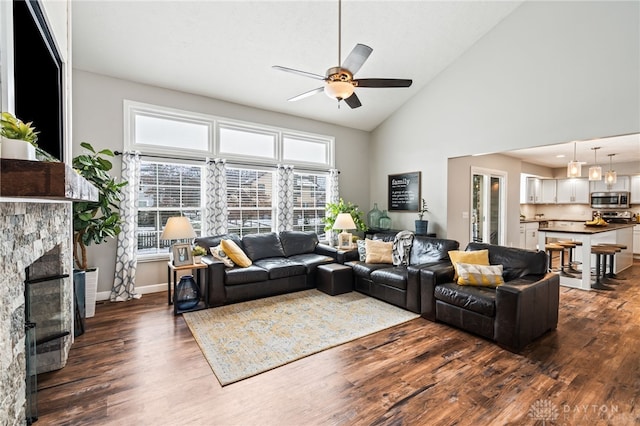 living room with ceiling fan, a stone fireplace, high vaulted ceiling, and dark hardwood / wood-style flooring