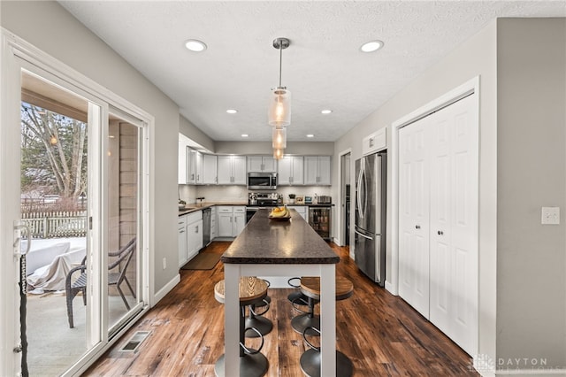 kitchen with a kitchen island, appliances with stainless steel finishes, dark hardwood / wood-style flooring, hanging light fixtures, and a textured ceiling