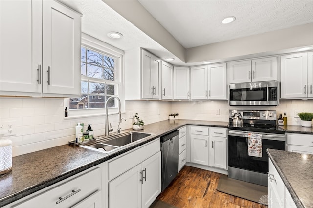 kitchen with dark wood-type flooring, sink, white cabinetry, stainless steel appliances, and backsplash