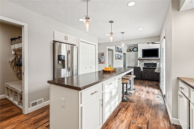 kitchen featuring a kitchen island, dark hardwood / wood-style floors, white cabinets, stainless steel fridge, and a kitchen bar