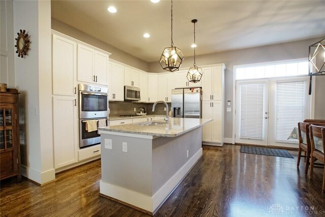 kitchen featuring appliances with stainless steel finishes, decorative light fixtures, white cabinetry, sink, and a kitchen island with sink