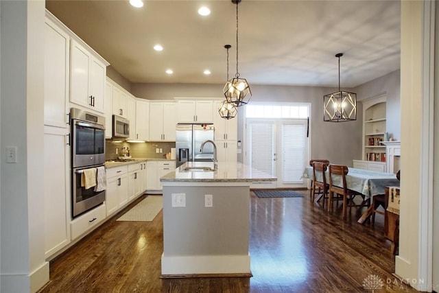 kitchen with stainless steel appliances, decorative light fixtures, a center island with sink, and white cabinets