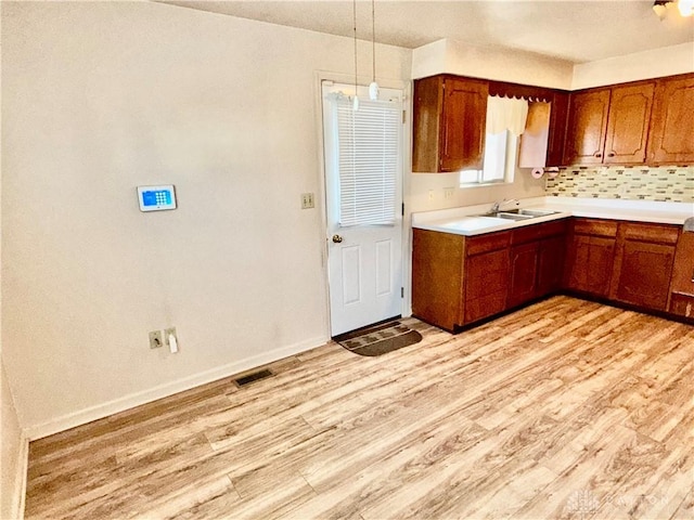 kitchen featuring sink, decorative backsplash, light hardwood / wood-style flooring, and hanging light fixtures