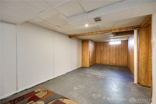 basement with a drop ceiling and wood walls